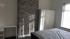 A room with a brick wall, a white wardrobe, a bed, and a window.