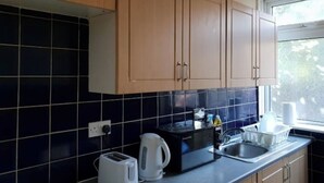 A kitchen with wooden cabinets, a black tiled backsplash, a microwave, a kettle, a toaster, and a sink.