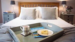 A neatly made bed with a tray containing a book, a mug, and a plate with food. - Scott Cottage - Luxury in the heart of Loch Lomond & The Trossachs (Stronachlachar)