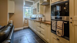 A modern kitchen with white cabinets, a black oven, and a window with a view of greenery. - Scott Cottage - Luxury in the heart of Loch Lomond & The Trossachs (Stronachlachar)