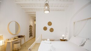 A minimalist bedroom with a large bed, a bedside table, a mirror, and a hanging light fixture. - My Rental Homes - Marvi House with shared pool (Mykonos)
