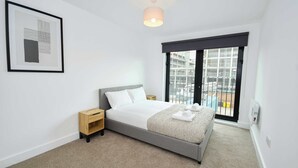 Ein modernes Schlafzimmer mit Bett, Nachttisch und einem Fenster mit Blick auf Gebäude.