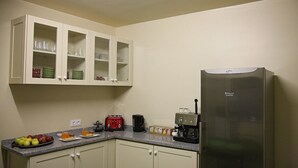 A kitchen with white cabinets, a stainless steel refrigerator, a toaster, a coffee maker, and a countertop with fruits and a glass of orange juice. - 29 Madeira Hostel (Funchal)