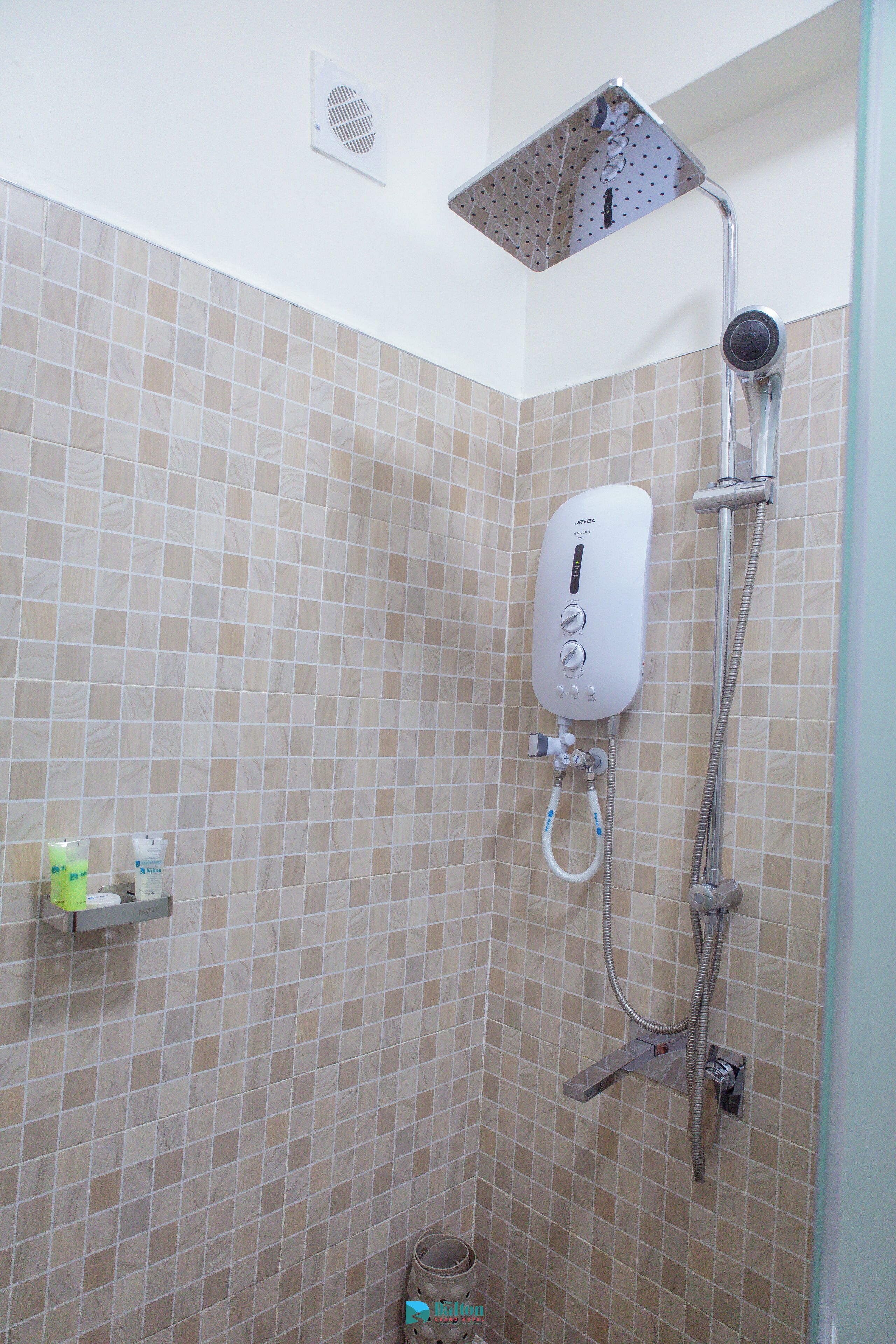 A shower area with a handheld showerhead, a wall-mounted control panel, and a small shelf with toiletries.