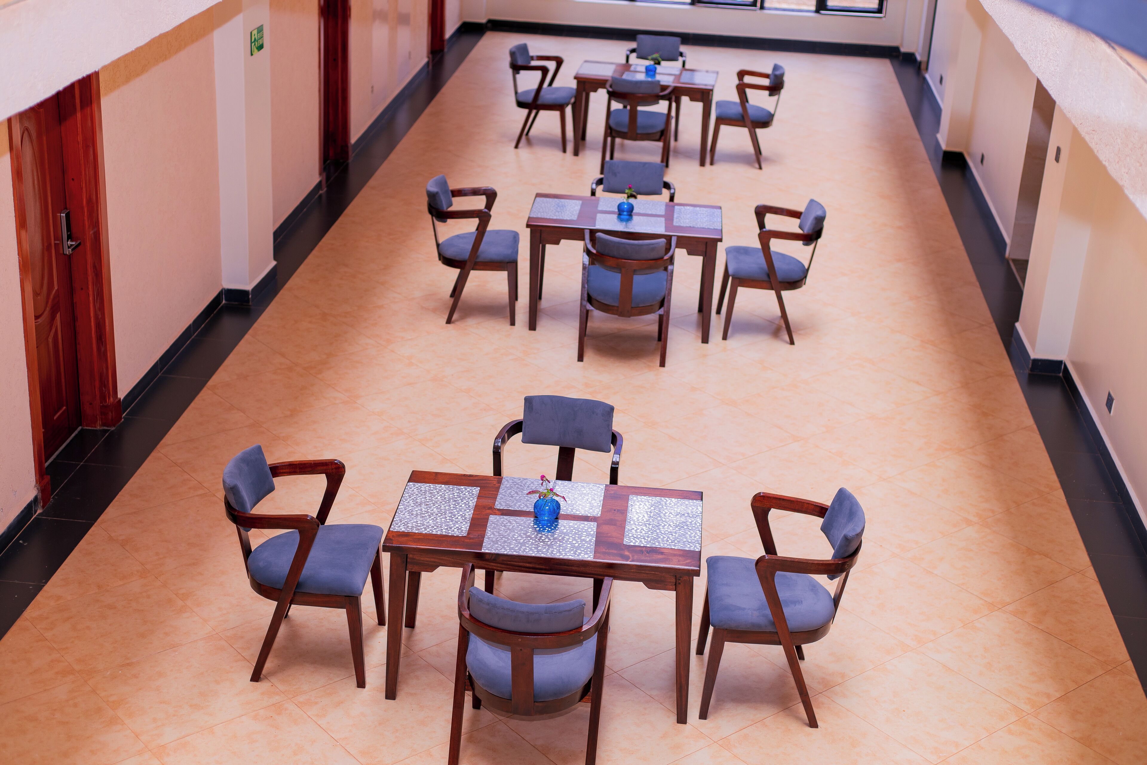 Un couloir d’hôtel avec de nombreuses tables et chaises, disposées en ligne le long des murs.