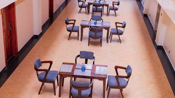 Un couloir d’hôtel avec de nombreuses tables et chaises, disposées en ligne le long des murs.
