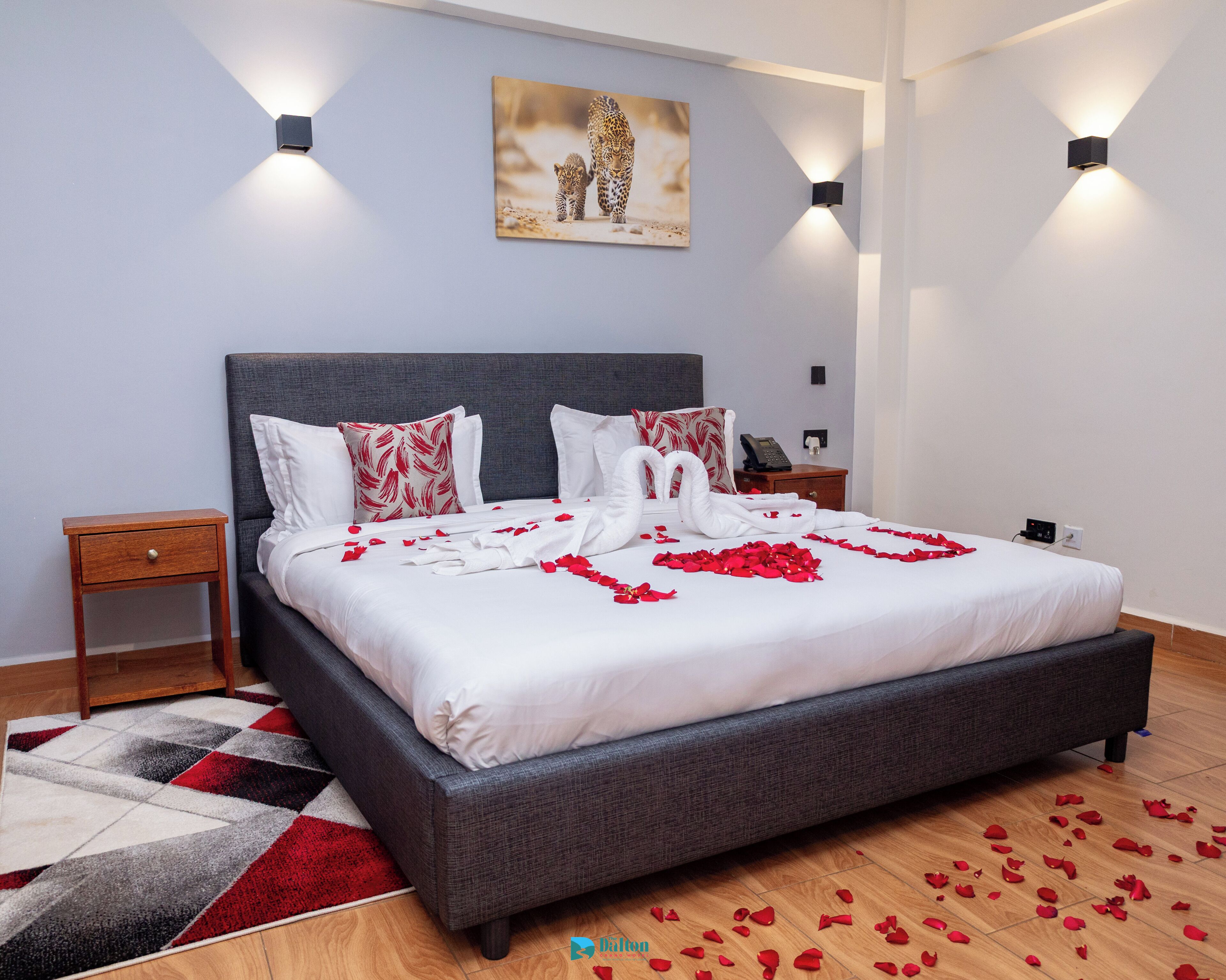 A neatly made bed with rose petals, a grey headboard, and a painting of a leopard on the wall.