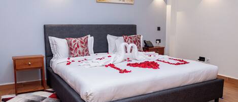 A neatly made bed with rose petals, a grey headboard, and a painting of a leopard on the wall.