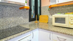 A kitchen with granite countertops, a microwave, a wooden cutting board, and white cabinets.