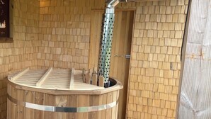 Un bain à remous en bois doté d’une structure métallique, d’un banc en bois et d’un mur en bois orné d’un motif en forme d’écailles.