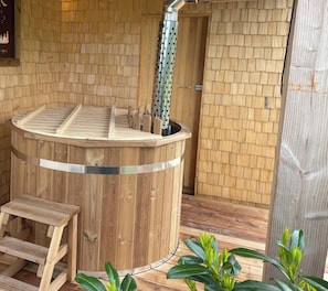 Un bain à remous en bois doté d’une structure métallique, d’un banc en bois et d’un mur en bois orné d’un motif en forme d’écailles.