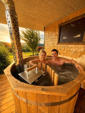A hot tub with wooden walls and a metal pole, surrounded by a wooden deck. - Luxury owl chalet with Finnish bath at Nature Cottage Vosges (Anould)