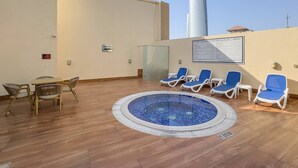 A rooftop pool area with lounge chairs, a small table, and a view of a tall building. - FIRST CLASS | 2BR | Cozy City Retreat (JLT)