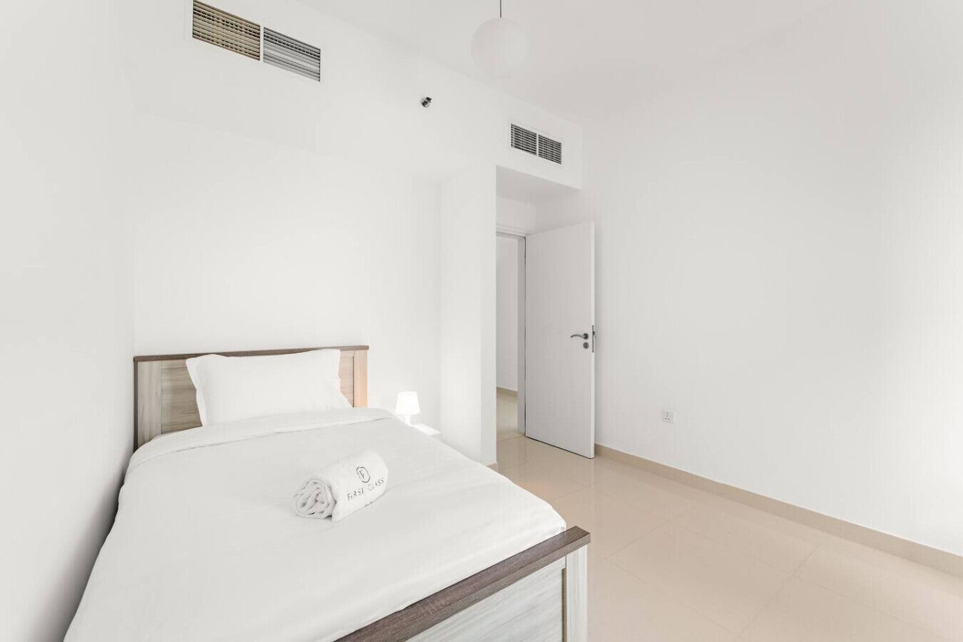Ein schlicht eingerichtetes Schlafzimmer mit Bett, Nachttischlampe und einer Tür zu einem anderen Raum.