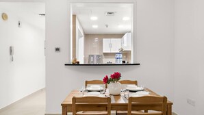 A dining area with a wooden table set for four, a vase with flowers, and a kitchen visible through a mirror. - FIRST CLASS | 2BR | Cozy City Retreat (JLT)