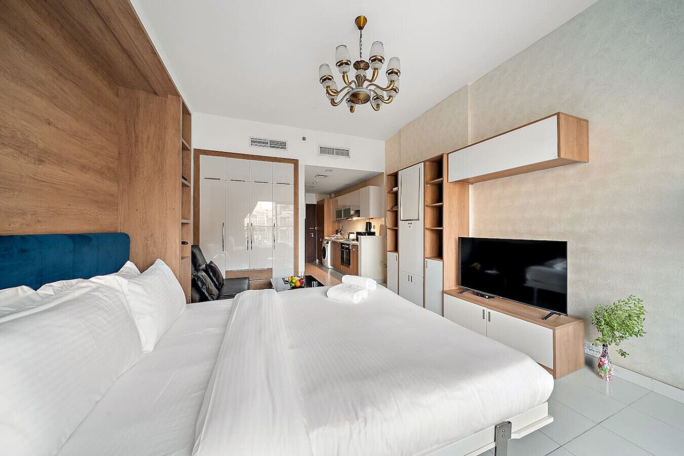 A modern hotel room with a large bed, built-in wardrobe, a flat-screen TV, and a small plant.