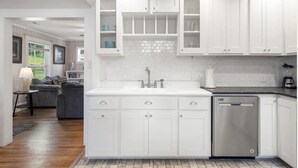 Een moderne keuken met witte kasten, een roestvrijstalen vaatwasser en een betegelde spatwand.