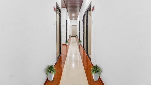 A long, narrow hallway with white walls and a wooden ceiling. There are potted plants on either side of the hallway. - Hotel K Parrk (Mumbai)