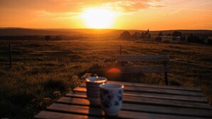 Un coucher de soleil sur un champ herbeux, avec un banc et une table sur laquelle se trouvent une tasse et une soucoupe.
