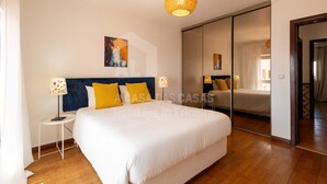 A hotel room with a large bed, a bedside table with a lamp, a mirror, and a painting on the wall.