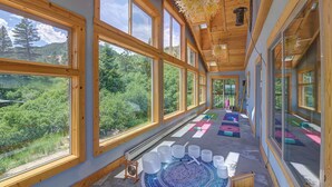 Una habitación amplia con ventanas grandes, techo de madera y vista a un área boscosa.