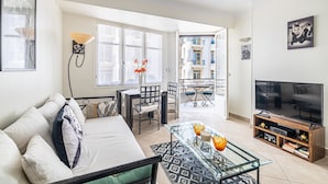 Un salon comprenant un canapé, une table basse en verre, un téléviseur et un balcon offrant une vue sur les immeubles.