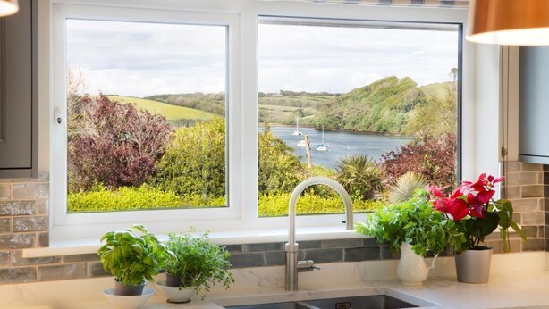 A kitchen with a large window offering a view of a river and hills. There are potted plants on the windowsill. - Luxury, spacious holiday home in St Mawes (St Mawes)