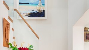 A staircase with wooden steps and white walls, a framed painting of a beach scene, a vase with flowers, and a hat on a wooden table. - Luxury, spacious holiday home in St Mawes (St Mawes)