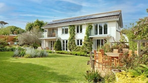 A two-story house with a garden, a patio with wooden furniture, and solar panels on the roof. - Luxury, spacious holiday home in St Mawes (St Mawes)