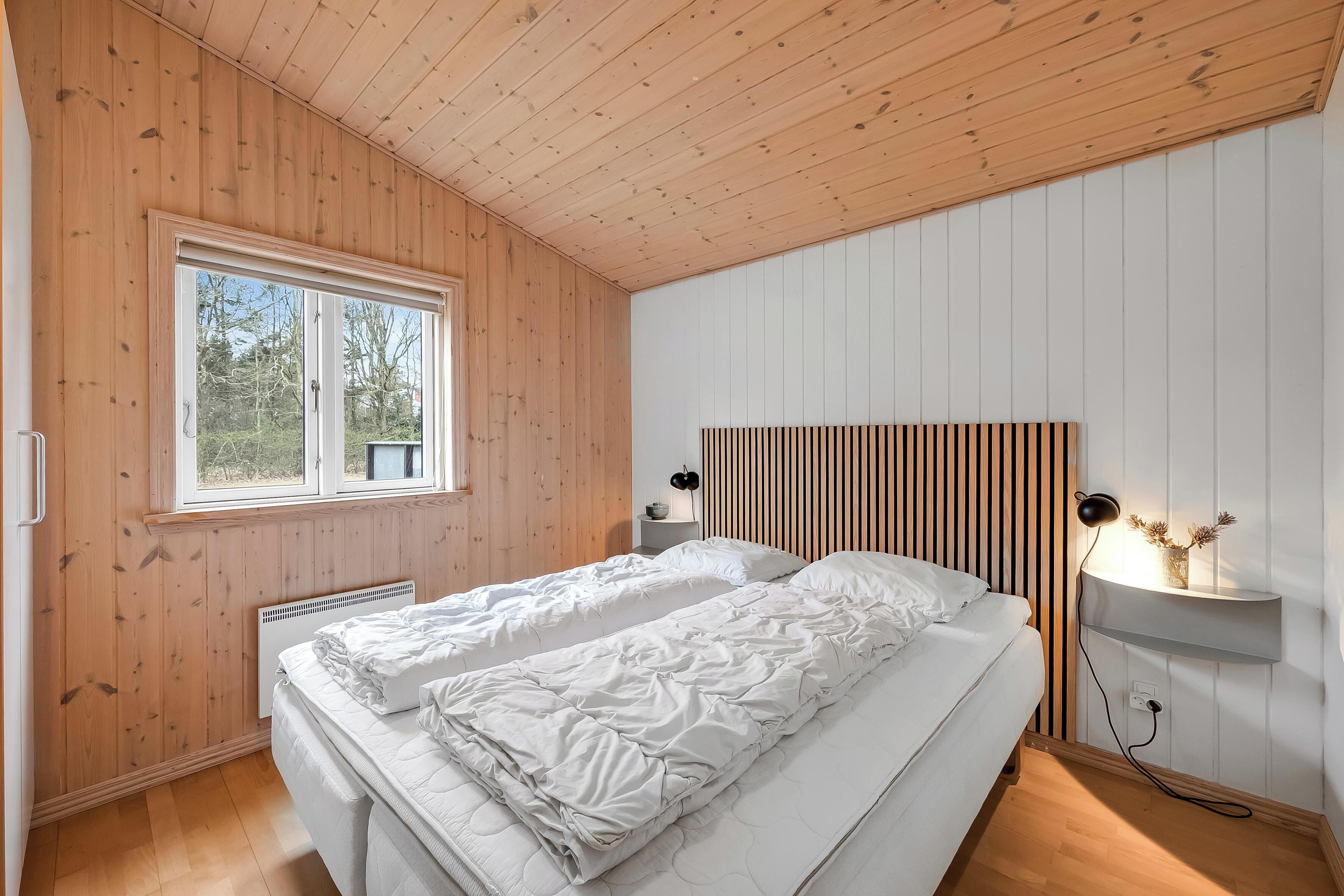 Un dormitorio con dos camas, una ventana, una mesita de noche con lámpara y un estante en la pared.