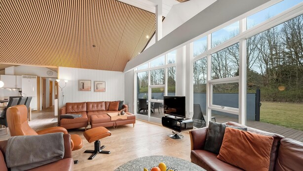 Un salon spacieux doté d’une grande fenêtre, d’un plafond en bois et d’un ensemble de meubles de salon moderne.