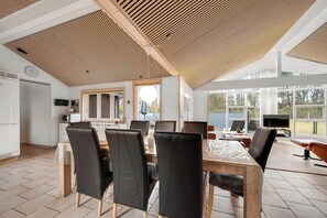 Een moderne keuken met een houten plafond, een eethoek met een grote tafel en stoelen, en uitzicht op de omgeving door grote ramen.