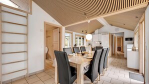 Une cuisine moderne avec des meubles blancs, un plafond en bois et un coin repas comprenant une table et des chaises.