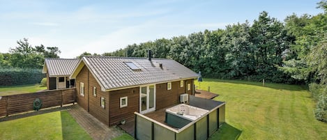 A two-story wooden house with a patio and a hot tub.