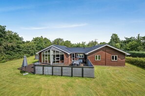 Een modern huis met een groot raam, een terras met tuinmeubilair en een verzorgd gazon.