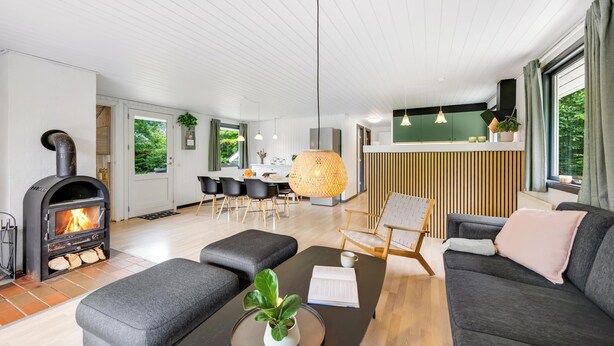 Una sala de estar moderna con chimenea, sofás grises, un comedor y una cocina con armarios de madera.