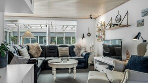 Una sala de estar moderna con un sofá modular, una mesa de centro redonda, un televisor de pantalla plana y una estantería.