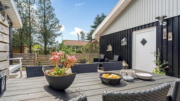 Un patio exterior con una mesa lista para comer, sillas de mimbre y una maceta con flores rosadas.