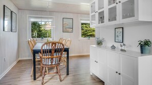Un comedor con una mesa y sillas de madera, muebles blancos con puertas de vidrio y cuadros en las paredes.