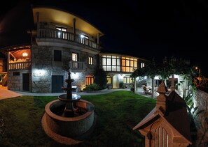 A multi-story stone building with a fountain in the courtyard, illuminated by exterior lights.