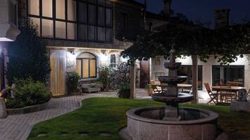 A courtyard with a stone fountain, outdoor seating, and a building with large windows and stone walls.