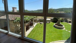 A view through a large window of a well-maintained garden with a lawn, a stone fountain, and outdoor seating.