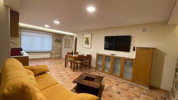 A living room with a sofa, a coffee table, a TV, and a dining area with chairs and a table.