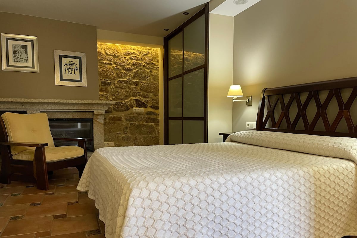 Habitación de hotel con cama, una silla, pared de piedra y cuadros en la pared.