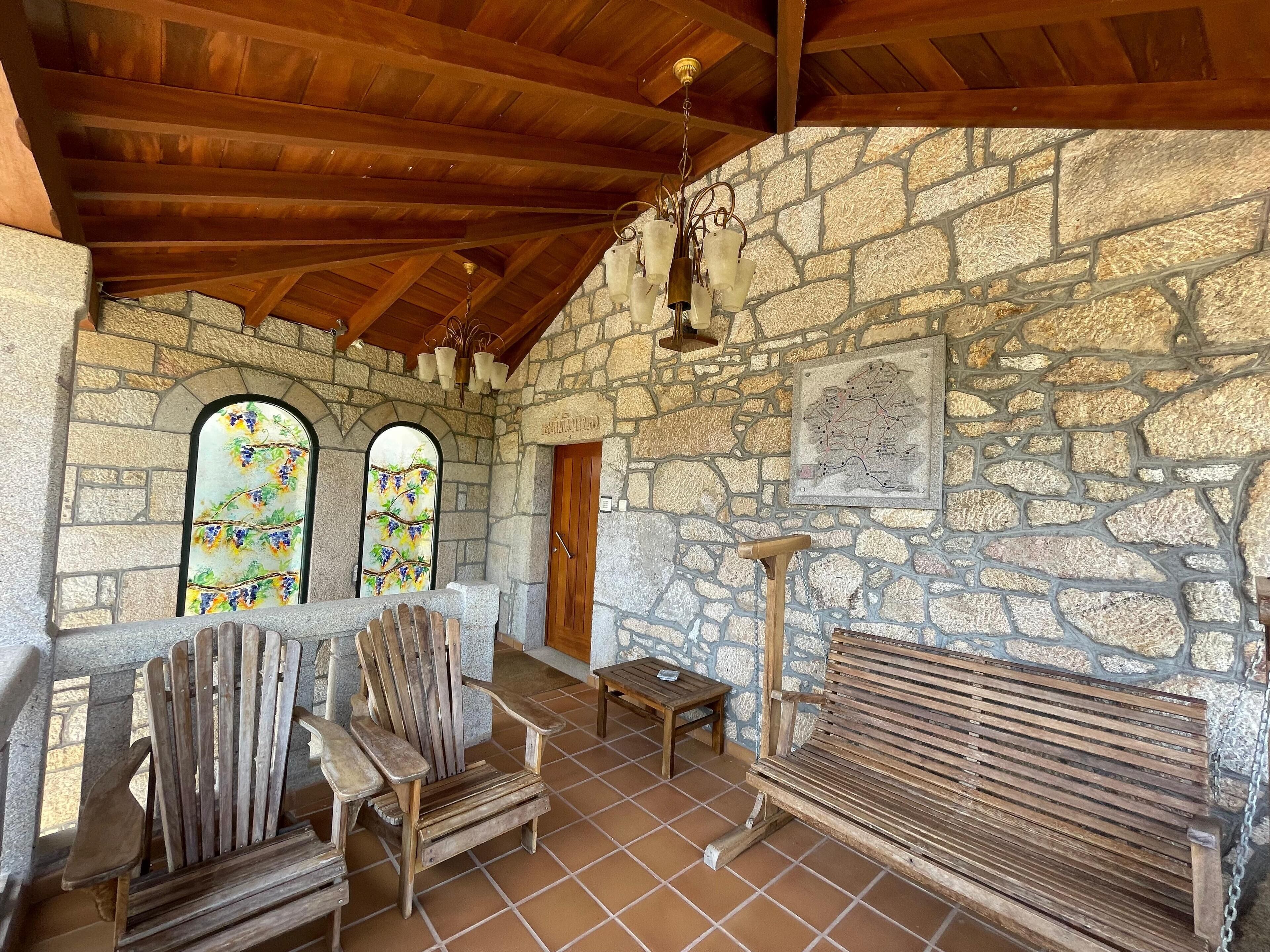 A rustic stone-walled room with wooden furniture, including a bench and chairs, and a map on the wall.