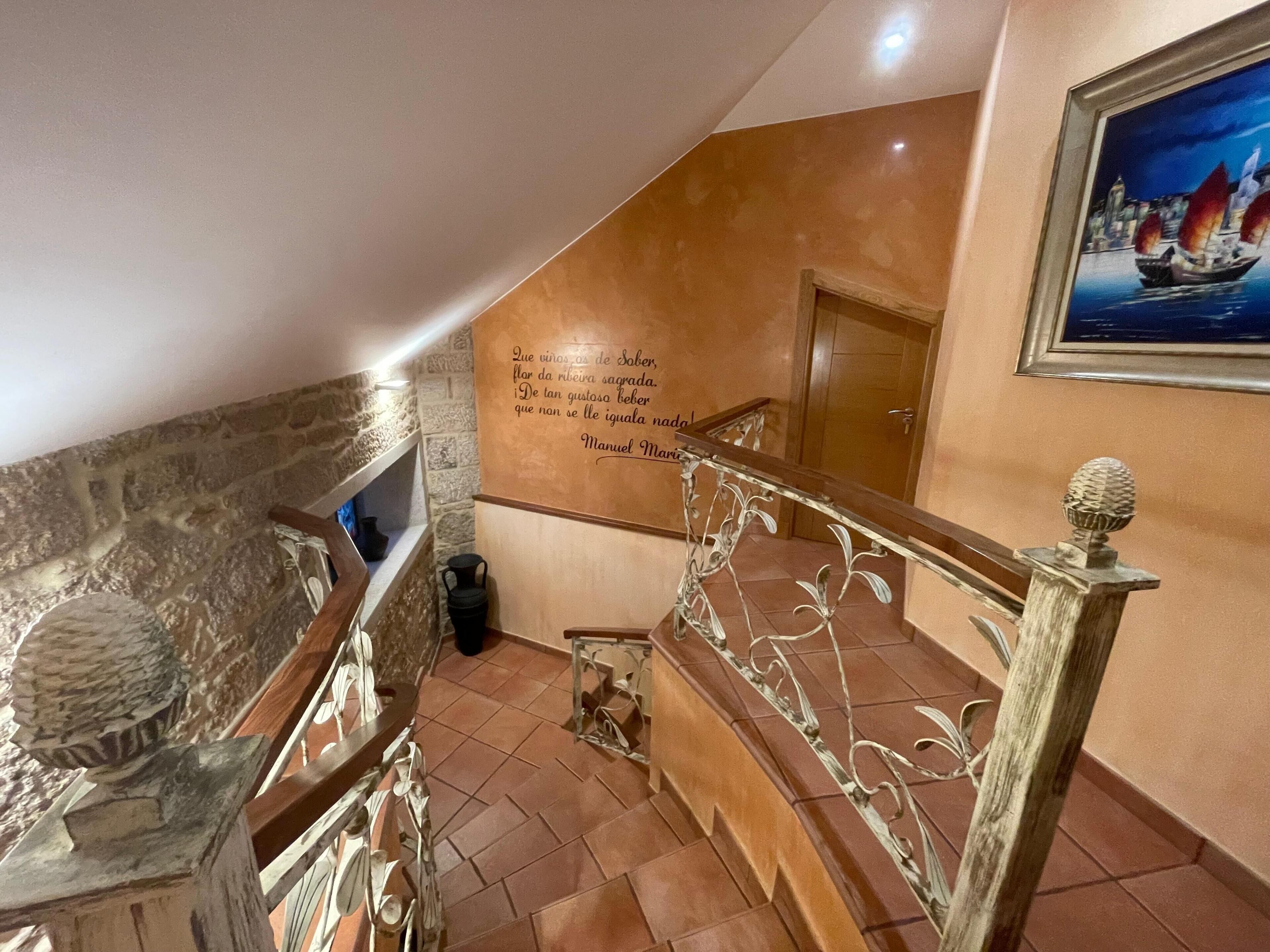 A staircase with a decorative railing, a stone wall, and a wall with a quote in Portuguese.