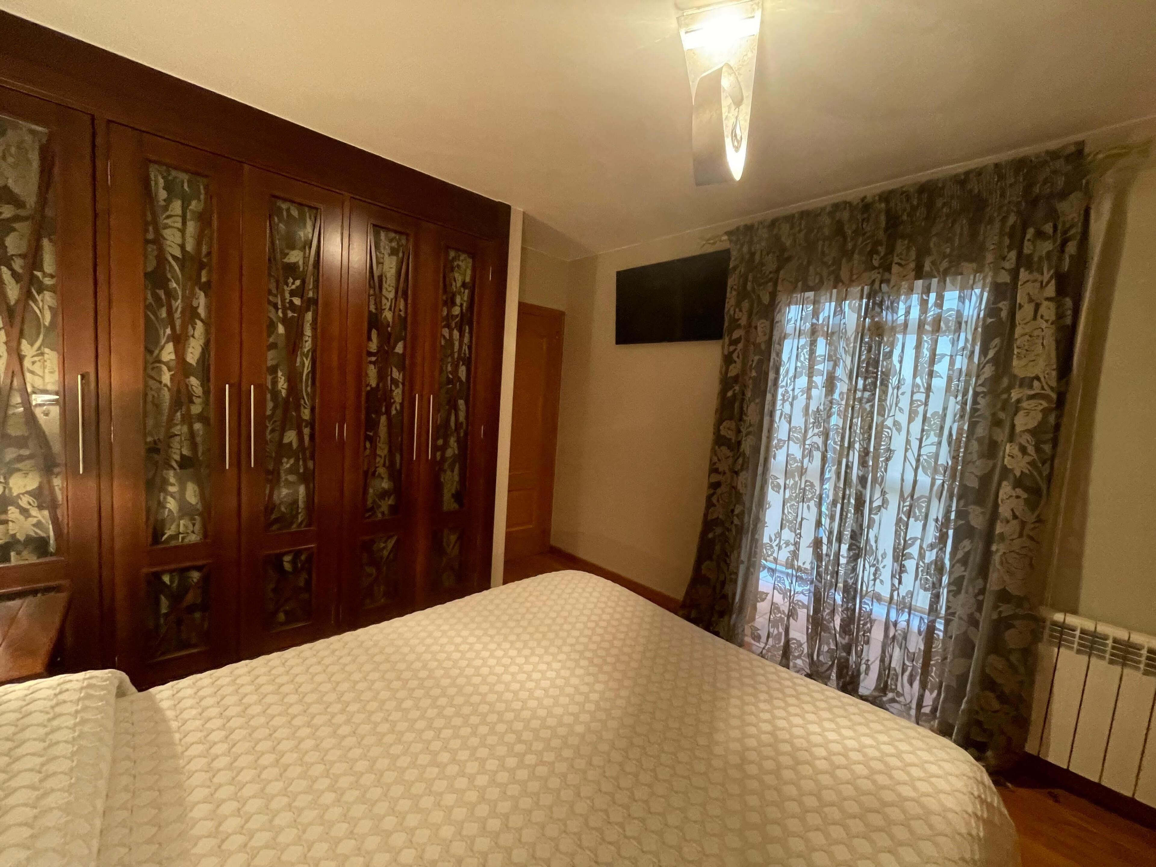 Ein Schlafzimmer mit Bett, Holzschrank und Vorhängen.
