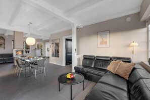 Ein modernes Wohnzimmer mit Ledersofa, Esstisch und Stühlen. Auf einem kleinen Tisch steht eine Obstschale, und eine Pendelleuchte hängt von der Decke.