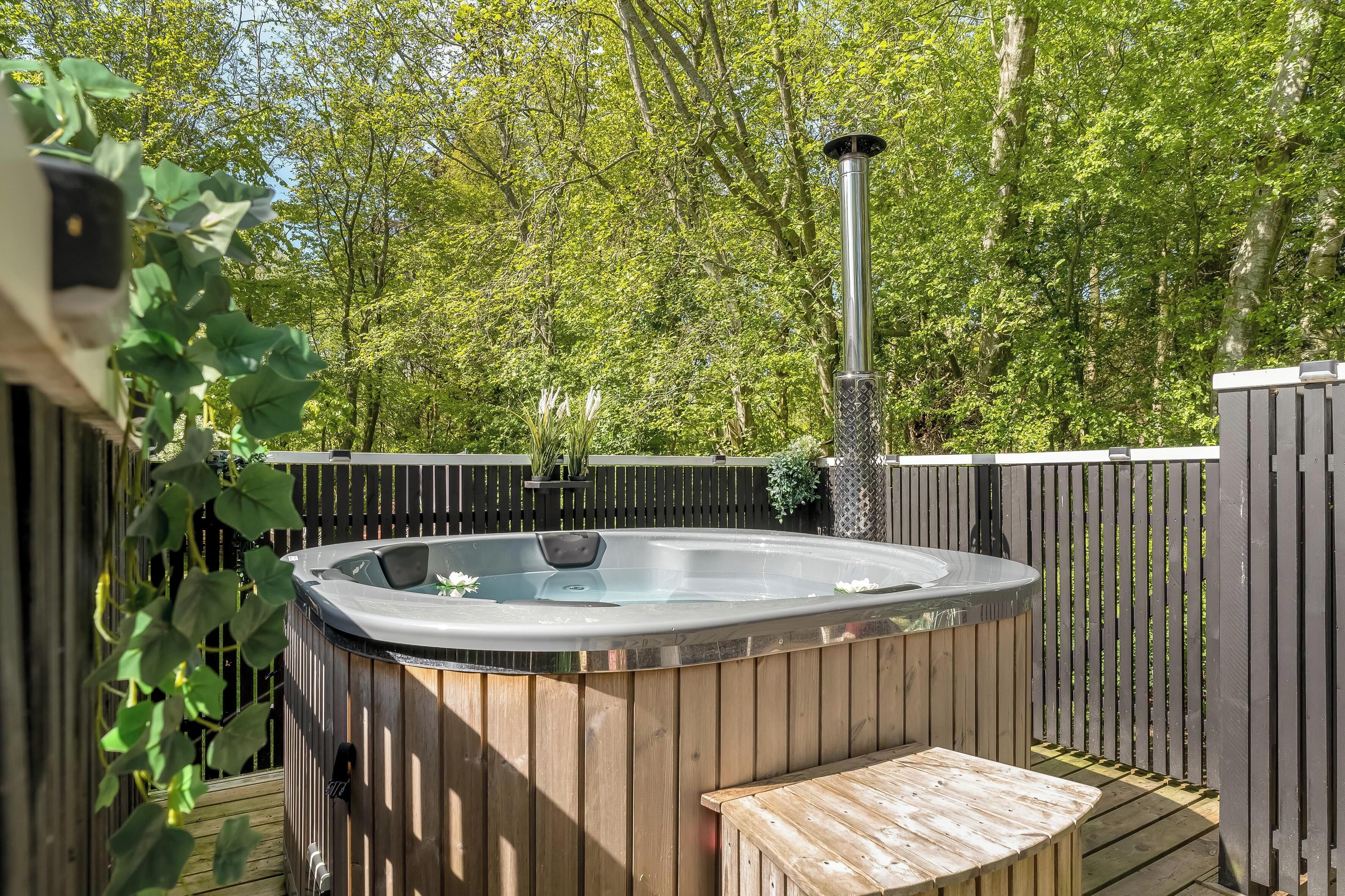 A hot tub with a wooden deck and a wooden fence, surrounded by greenery.
