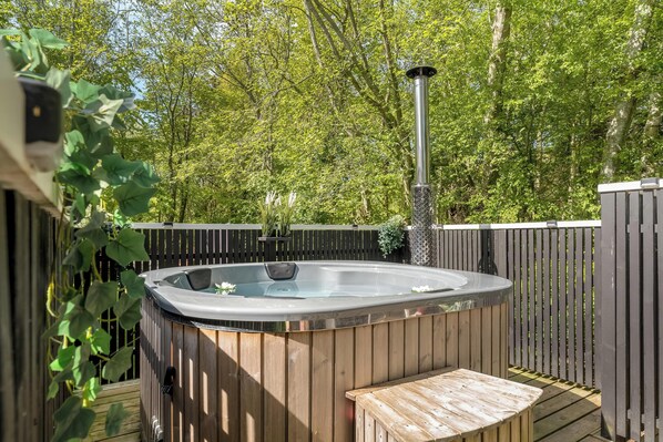A hot tub with a wooden deck and a wooden fence, surrounded by greenery.